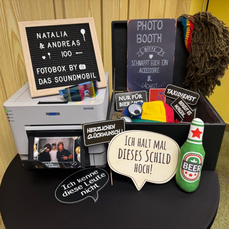 fotobox event setup dekorierter tisch mit fotoautomatendrucker, schildern und lustigen requisiten für eine feier.
